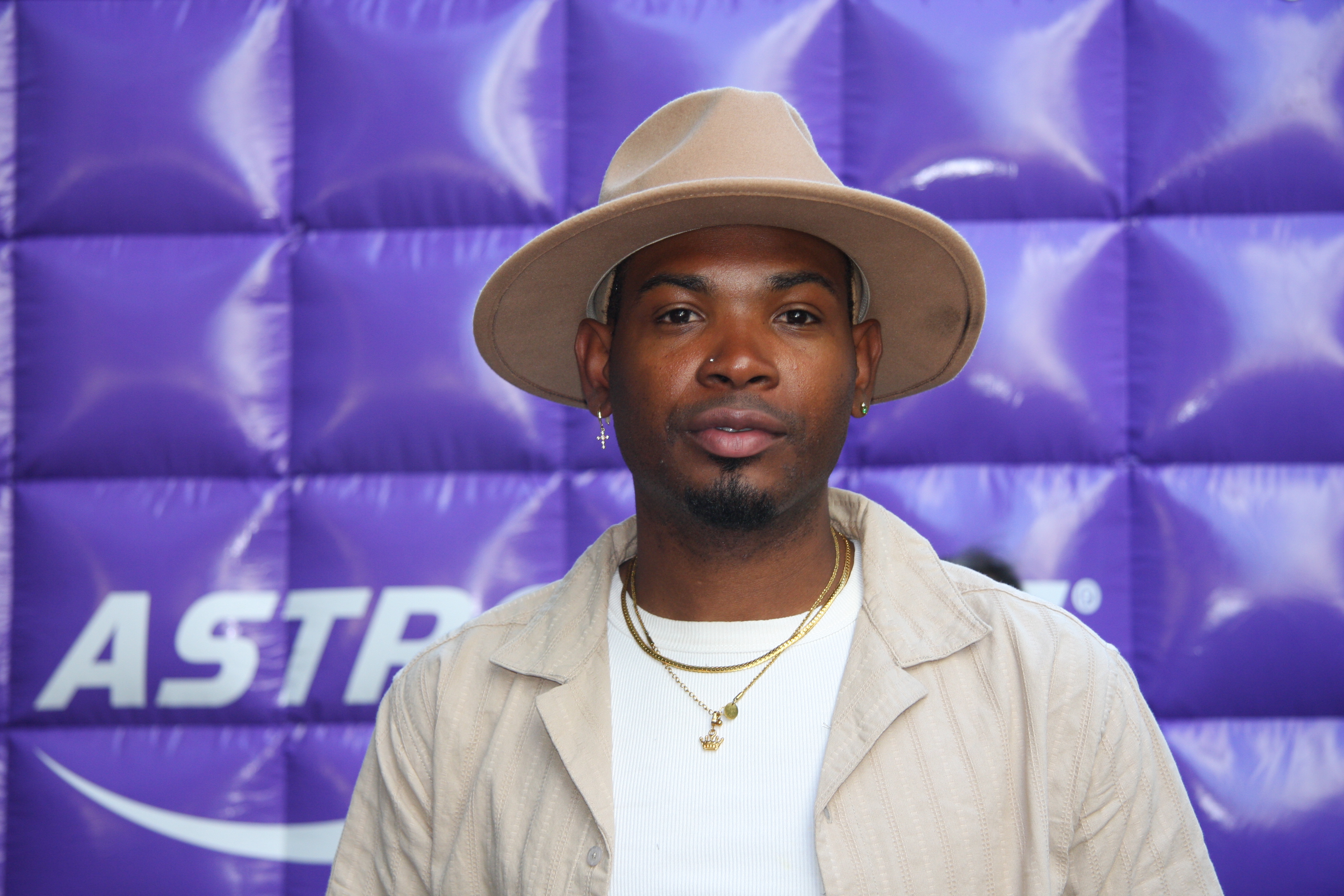 A Black man wearing a fedora against a purple backdrop