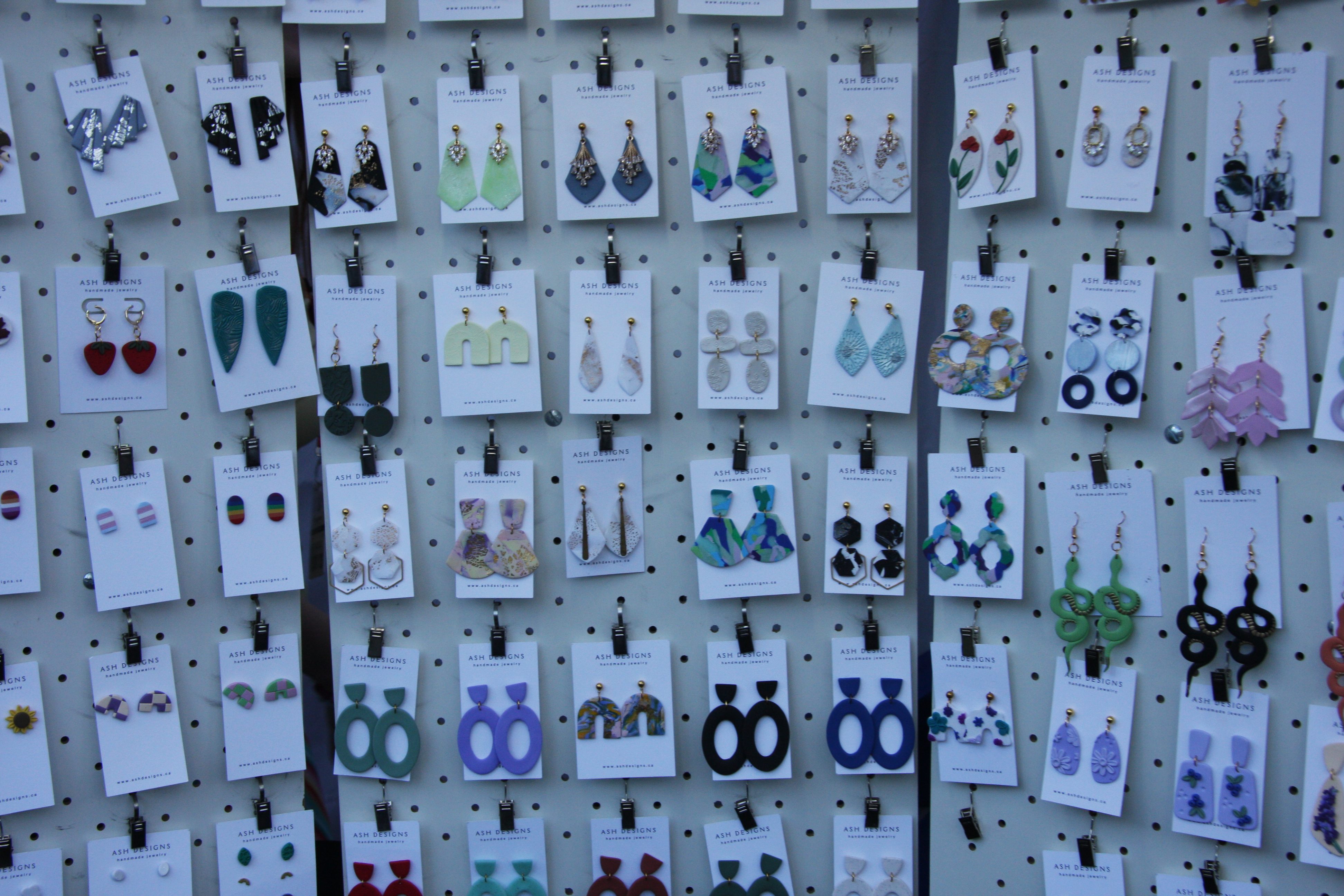 Rows of handmade polymer clay earrings displayed on cards at Ash Designs' vendor booth.